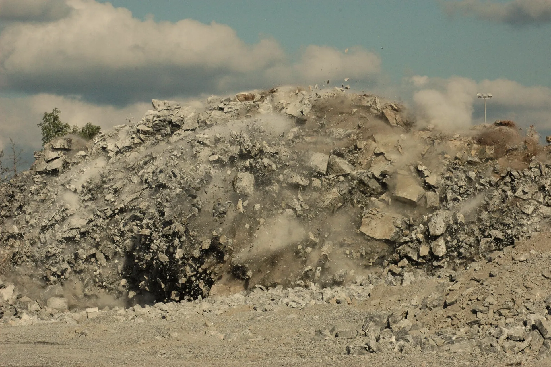 Controlled blast throwing rock and dust on a hard-rock bench